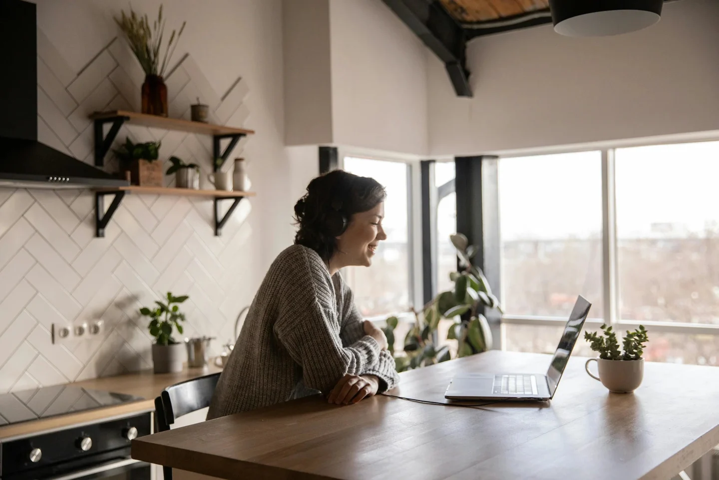 A woman at her kitchen table, looking out of the window beside her laptop